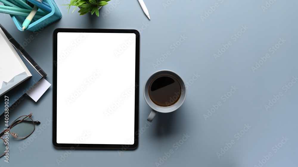 Overhead shot of mock up tablet computer, coffee cup, notebook and stationery on gray desk. Blank screen for graphics display montage. Overhead shot of mock up tablet computer, coffee cup, notebook and stationery on gray desk. Blank screen for graphics display montage.