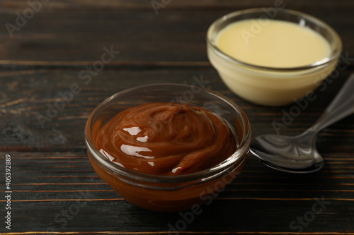 Spoons and bowls with condensed milk on wooden background