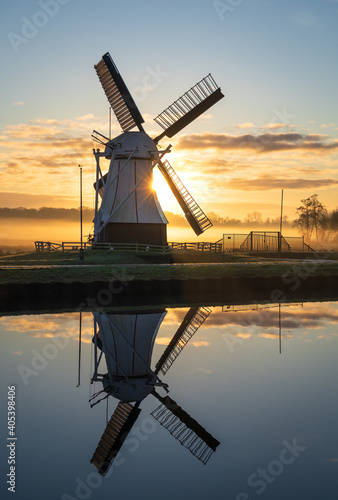Foggy sunrise at a Dutch windmill reflected in a canal.