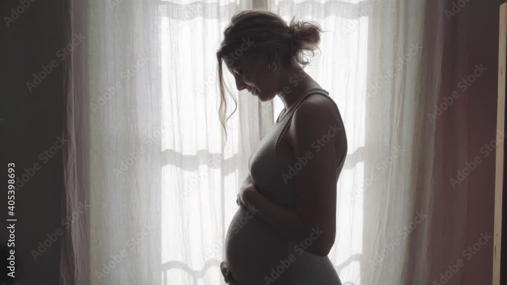 Pregnant woman stroking baby belly in front of window at home Pregnant woman stroking baby belly in front of window at home