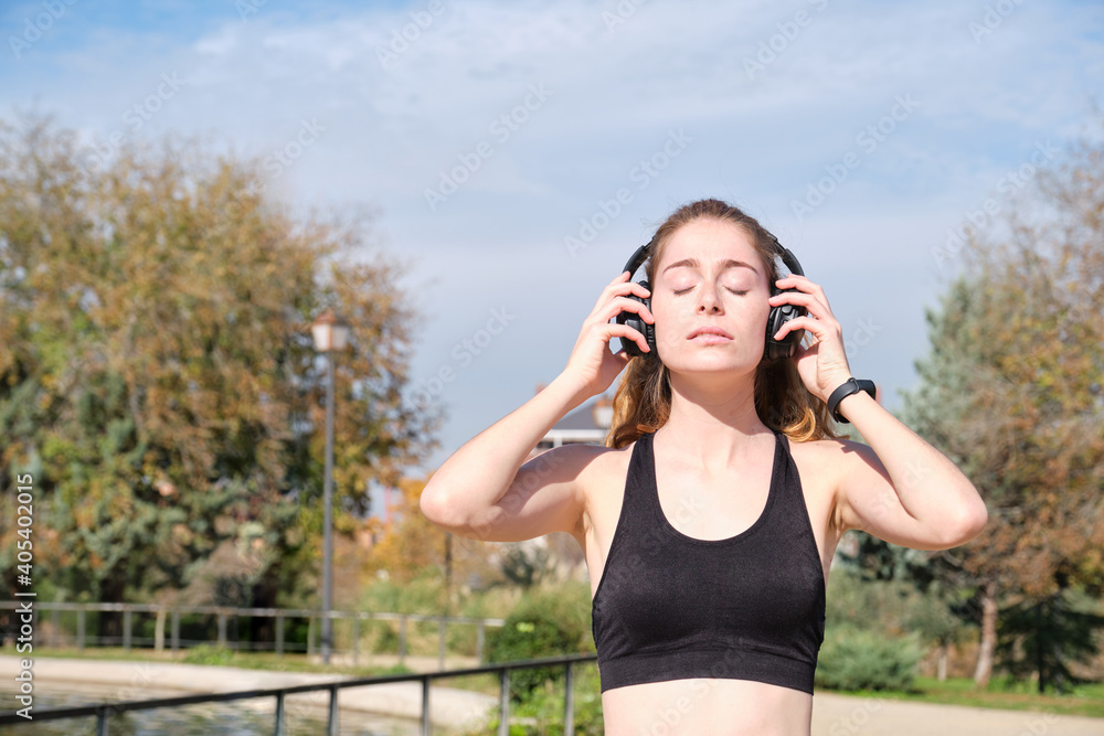 Redhead caucasian woman putting on her headphones. Fitness and sport outdoor.
