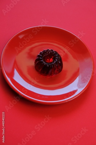 Red jelly dessert in a red round plate on a bright red background . A gelatinous dietary low calorie vegetarian dessert. Vegan dessert. Low Calorie  Sweets