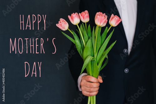 Man giving a bouquet of pink flowers tulips. Greeting card with text Happy mother's day