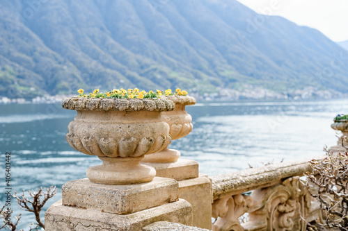 An architectural flowerpot on a stone fence against the backdrop of water and mountains.