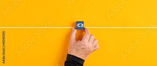 Male hand holds a blue wooden cube with logistics delivery truck icon on yellow background.