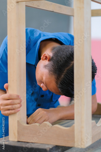 Young carpenter in work clothes assambling components of console table in workshop. photo