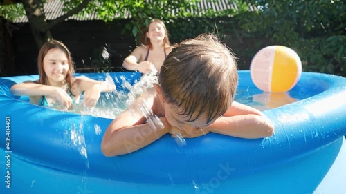 Portrait of upset little boy sitting on the poolside while family playing and having fun. Concept of happy and cheerful summer holidays and vacation