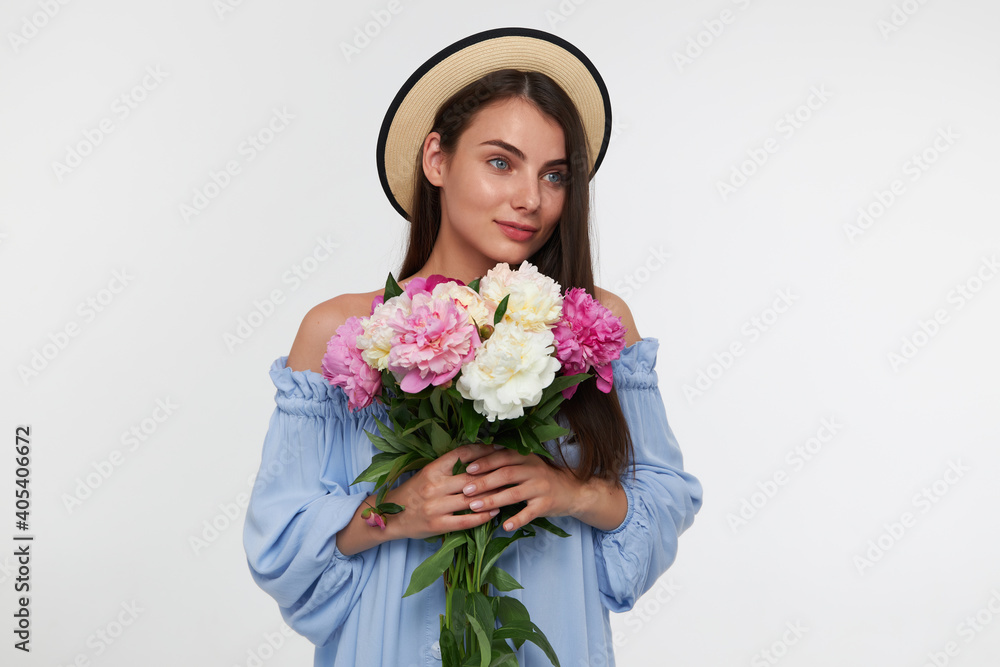 Young lady, pretty woman with long brunette hair. Wearing a hat and blue pretty dress. Holding a bouquet of beautiful flowers. Watching to the right at copy space over white background Young lady, pretty woman with long brunette hair. Wearing a hat and blue pretty dress. Holding a bouquet of beautiful flowers. Watching to the right at copy space over white background