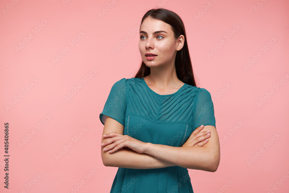 Teenage girl, happy looking woman with brunette long hair. Folding hands on a chest. Wearing emerald dress. Watching to the left at copy space over pastel pink background Teenage girl, happy looking woman with brunette long hair. Folding hands on a chest. Wearing emerald dress. Watching to the left at copy space over pastel pink background