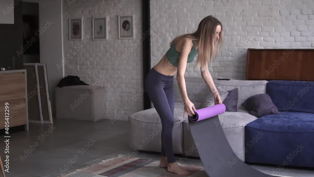 Young sporty girl unfolding fitness mat on floor at home Young sporty girl unfolding fitness mat on floor at home