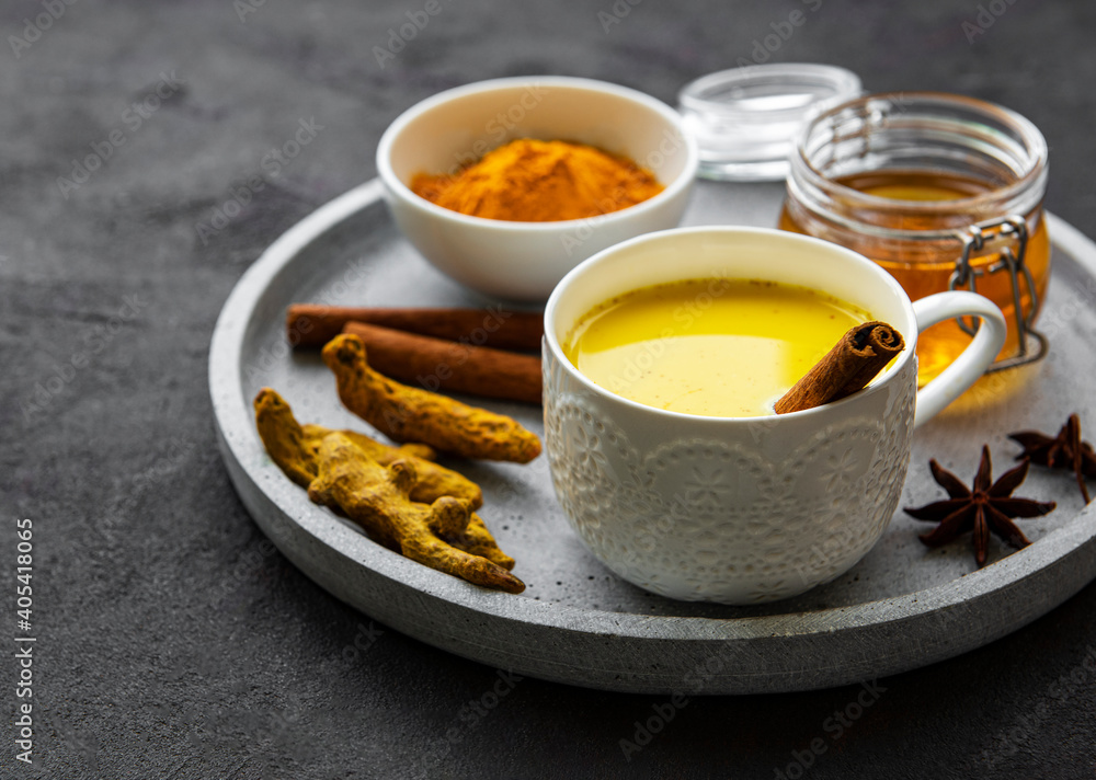 Yellow turmeric latte drink. Golden milk with cinnamon, turmeric, ginger and honey over black concrete background. Yellow turmeric latte drink. Golden milk with cinnamon, turmeric, ginger and honey over black concrete background.