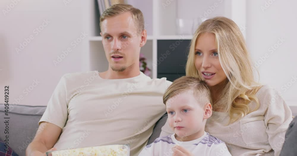 Smiling young family with preschooler son sit relax on sofa watching movie on tv eating popcorn, happy parents rest at home with little kid enjoy weekend together, have fun in living room. Smiling young family with preschooler son sit relax on sofa watching movie on tv eating popcorn, happy parents rest at home with little kid enjoy weekend together, have fun in living room.
