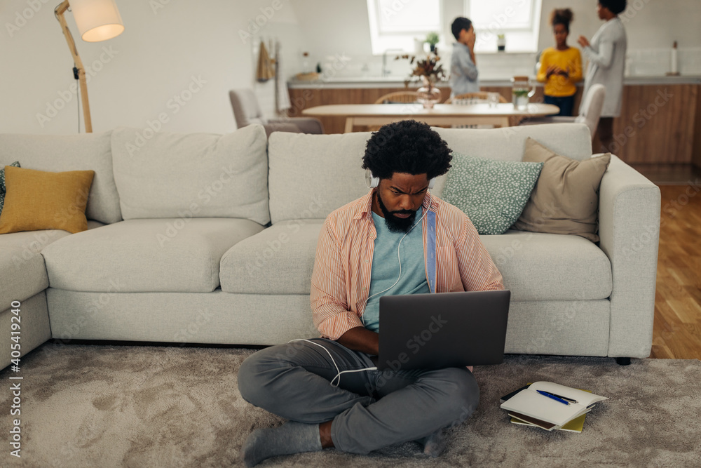 Young black man with earphones sitting on the floor and using laptop Young black man with earphones sitting on the floor and using laptop