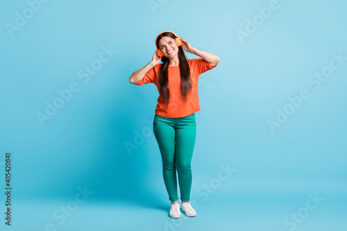 Fototapeta Naklejka Na Ścianę i Meble -  Full length photo of cheerful lady look empty space hands touch headphones isolated on blue color background