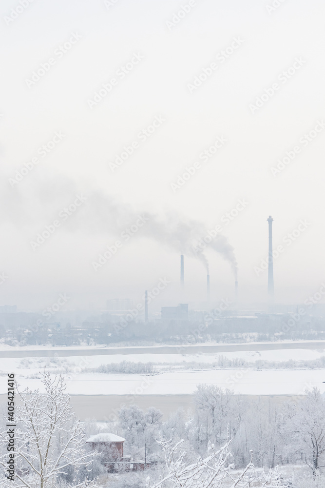 Winter cityscape - high pipes of a power plant and smoke against the sky on a frosty foggy day