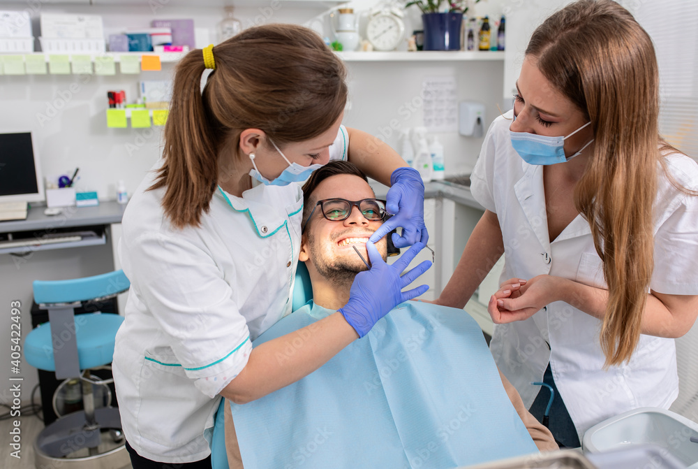 Obraz premium Female dentist with an assistant polishes teeth to a male patient in the dental clinic.