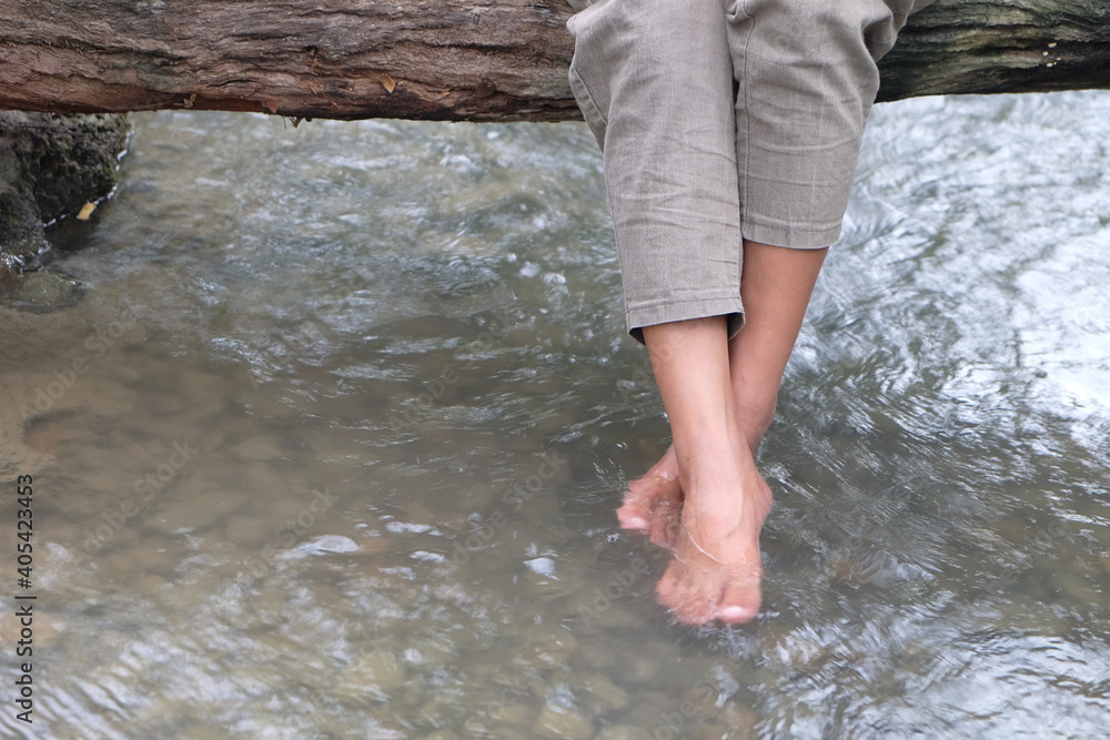 Legs of a woman in pants who sitting on a wood bridge and swinging her feet in a river Legs of a woman in pants who sitting on a wood bridge and swinging her feet in a river
