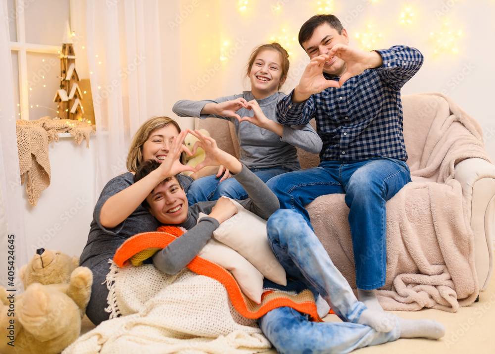 portrait of a family sitting on a sofa at home, four people having fun together, showing heart shape with their hands
