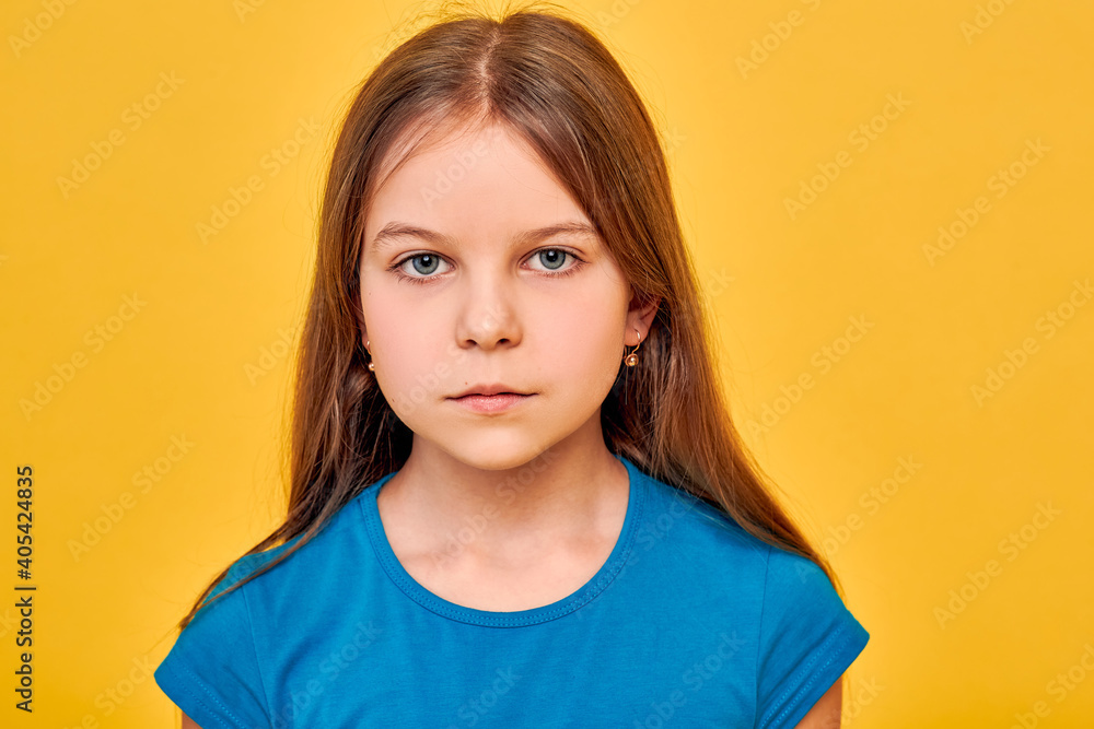 Fototapeta premium Little girl wearing a blue t-shirt, caucasian ethnicity, serious and looking at the camera, on fortune gold background