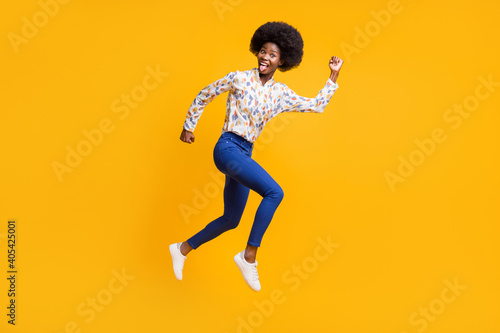 Full size profile side photo of brunette girl wear white print shirt blue pants jump run crazy isolated on yellow color background