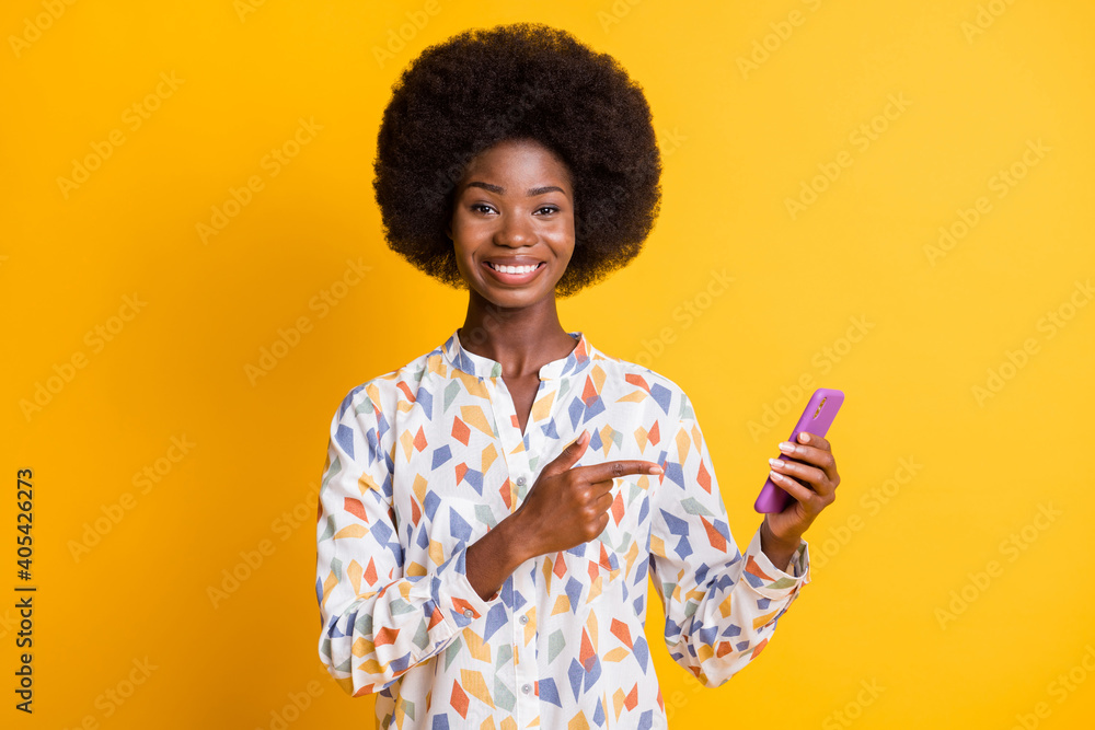 Photo of charming dark skin lady dressed casual outfit holding pointing finger modern device isolated yellow color background Photo of charming dark skin lady dressed casual outfit holding pointing finger modern device isolated yellow color background