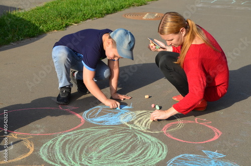 Child drawing sun and house on asphalt in a park on the playground or sidewalk, happy childhood, summer vacation, entertainment for children