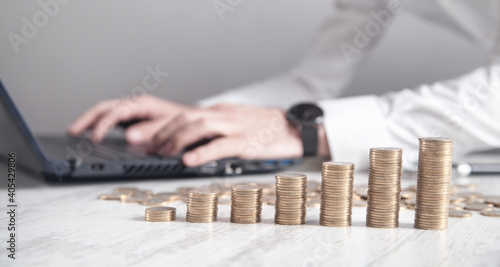 Stack of coins on the desk. Businessman working with laptop
