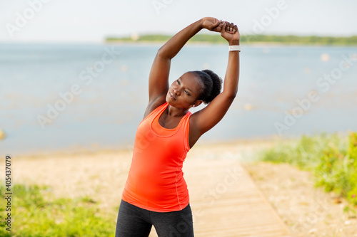 fitness, sport and healthy lifestyle concept - young african american woman stretching outdoors