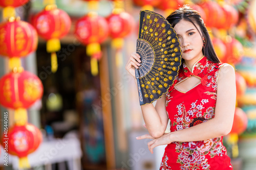 Portrait beautiful smiles Asian young woman wearing red traditional Chinese cheongsam decoration and holding a Chinese Fanning for Chinese New Year Festival at Chinese shrine in Thailand