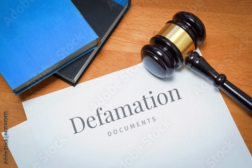 Defamation. Document with label. Desk with books and judges gavel in a lawyer's office. photo