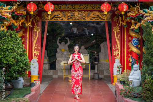 Portrait beautiful smiles Asian young woman wearing red traditional Chinese cheongsam decoration for Chinese New Year Festival at Chinese shrine in Thailand © Thinapob