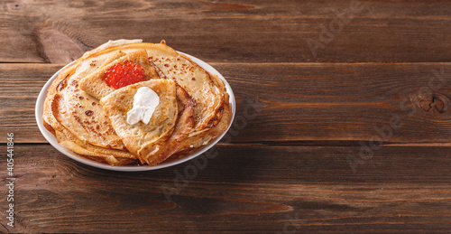 Traditional Russian Crepes Blini stacked in a plate with red caviar, fresh sour creamon dark wooden table. Maslenitsa traditional Russian festival meal. Long wide banner. Space for text photo