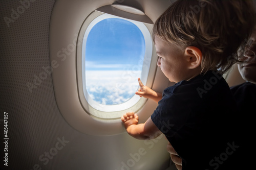cute toddler points his finger at the sky through the window. first flight concept, traveling with children. © Maria