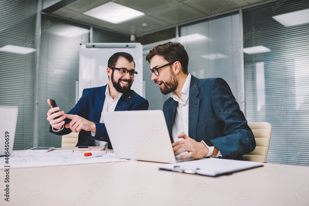 Cheerful businessman showing funny news to colleague during business meeting Cheerful businessman showing funny news to colleague during business meeting