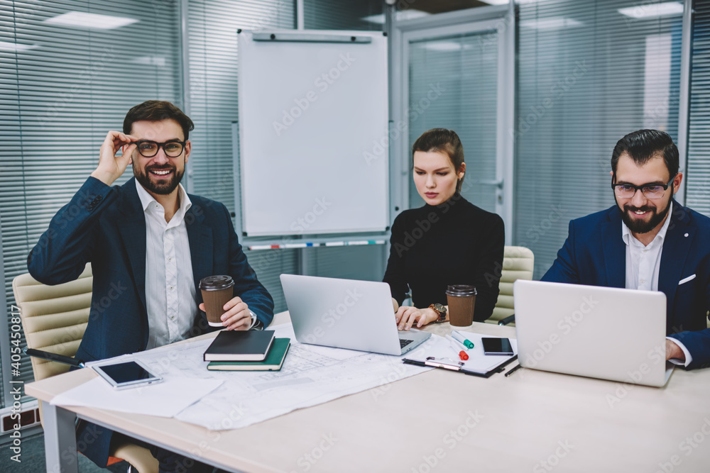 Happy man touching glasses while working with colleagues Happy man touching glasses while working with colleagues