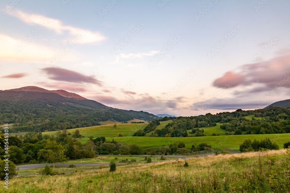 Landscape of grassed hills with the road serpentine ot the foreground and expressive soft clouds on the sky at dusk