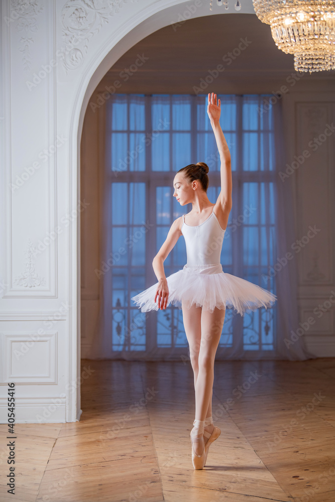 young slender ballerina in white tutu dances on pointe shoes in a spacious, bright room with large windows. young slender ballerina in white tutu dances on pointe shoes in a spacious, bright room with large windows.