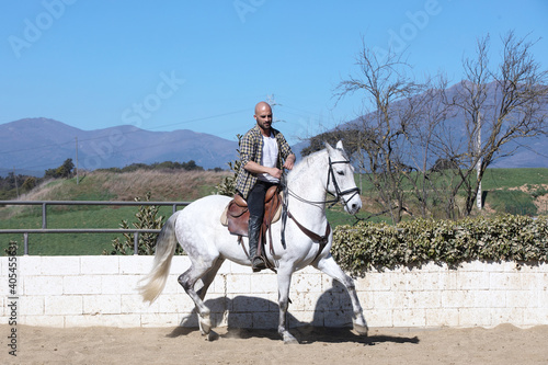 Young guy in casual outfit riding white horse on sandy ground © 2Design