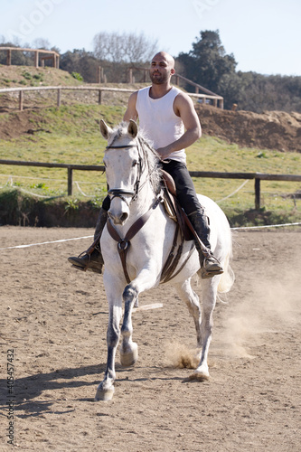 Young guy in casual outfit riding white horse on sandy ground © 2Design