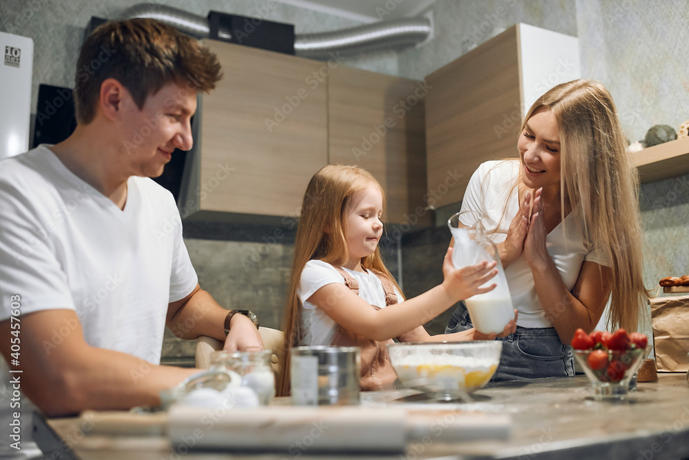 A full multicultural family with an adorable daughter gathered in a modern kitchen, preparing pancakes together. Making cake mix, pouring milk, socializing pleasure and culinary hobby A full multicultural family with an adorable daughter gathered in a modern kitchen, preparing pancakes together. Making cake mix, pouring milk, socializing pleasure and culinary hobby