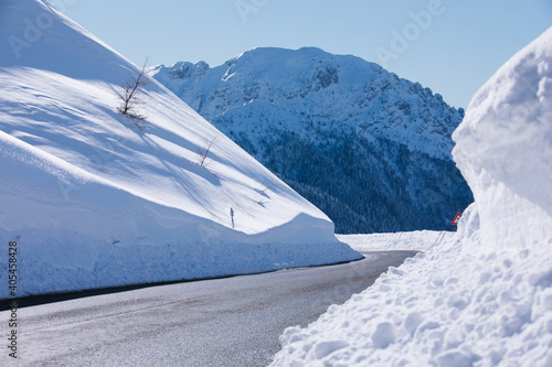 Empty deserted road on the sides of snowdrifts against the backdrop of snow-capped mountains and trees. Winter scenery.