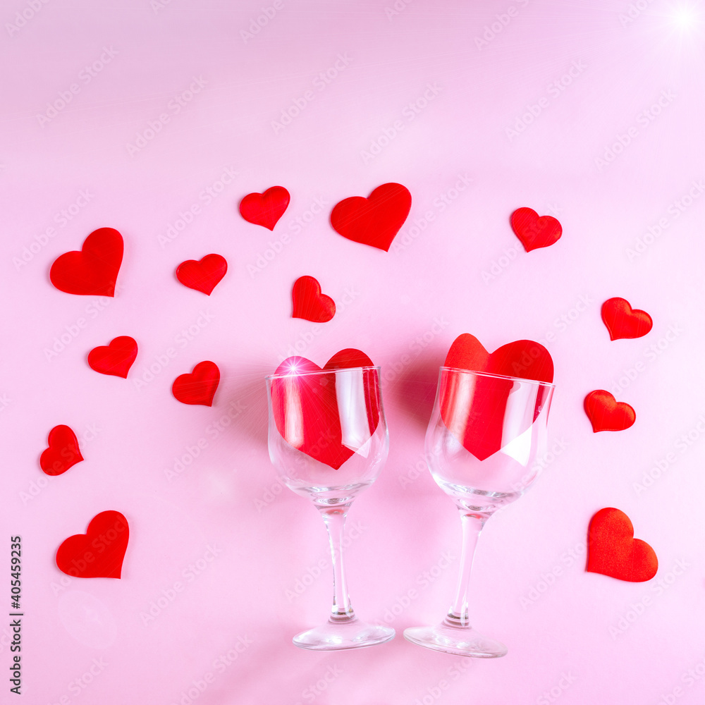Happy Valentine's Day greetings. Two wine glasses with red hearts on a pink background decorated with red heart shapes, flat lay, top view. Symbol of love, date, engagement