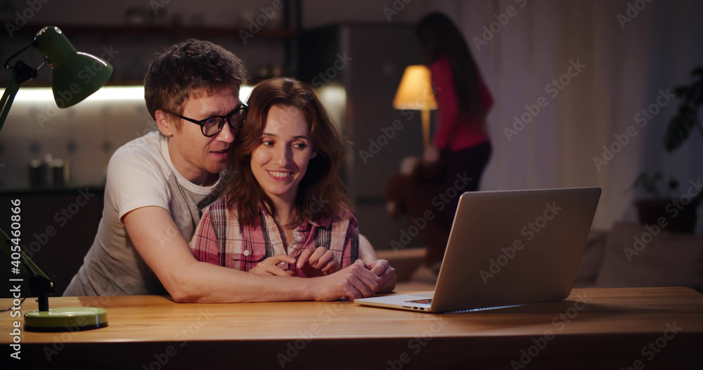 Happy couple surfing internet on laptop with little daughter playing on background Happy couple surfing internet on laptop with little daughter playing on background