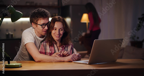 Happy couple surfing internet on laptop with little daughter playing on background