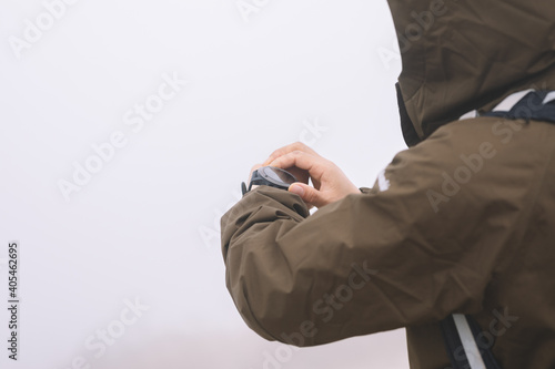Woman hiker checking the altitude on her smartwatch at foggy mountain top