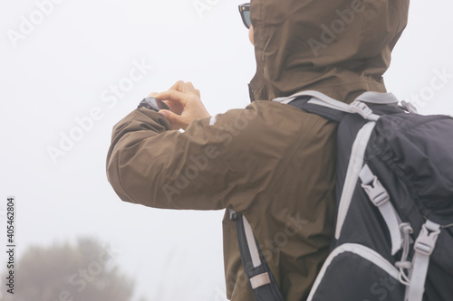 Woman hiker checking the altitude on her smartwatch at foggy mountain top