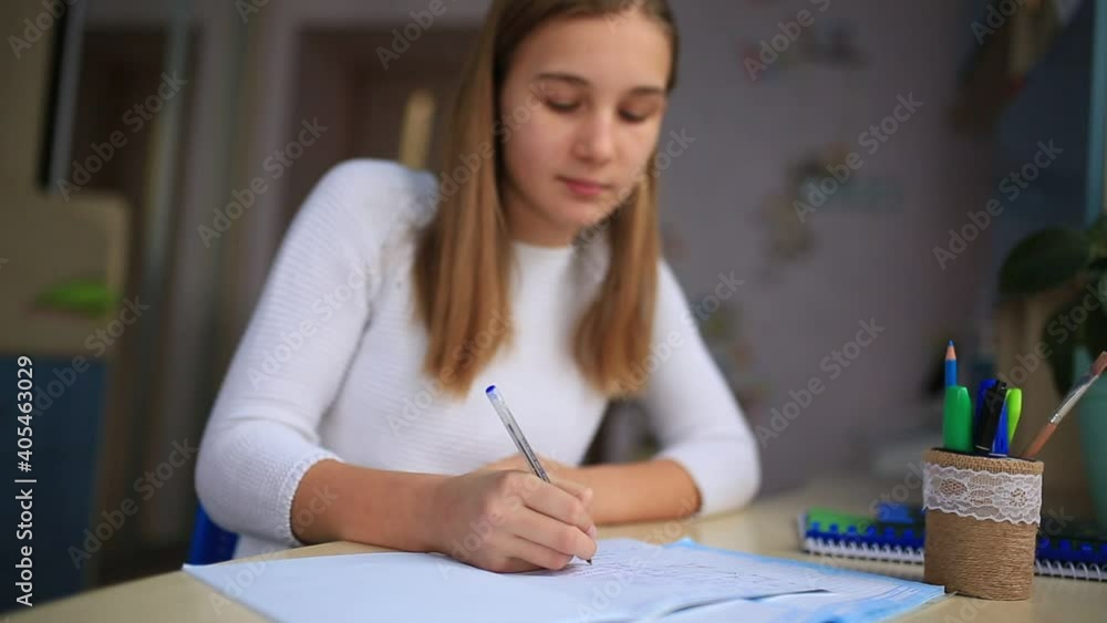 Beautiful schoolgirl studying at home doing school homework. Training books and notebook on the table. Distance learning online education Beautiful schoolgirl studying at home doing school homework. Training books and notebook on the table. Distance learning online education