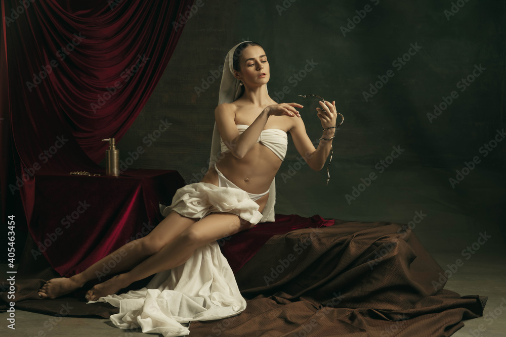 Suffering. Modern remake of classical artwork with coronavirus theme - young medieval woman on dark background posing with golden medicine, pills. Concept of coronavirus, pandemic, creativity.