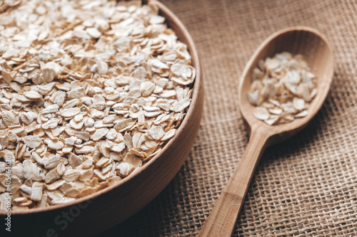 Dry oatmeal in a wooden bowl and spoon on a linen fabric background. Copy, empty space for text