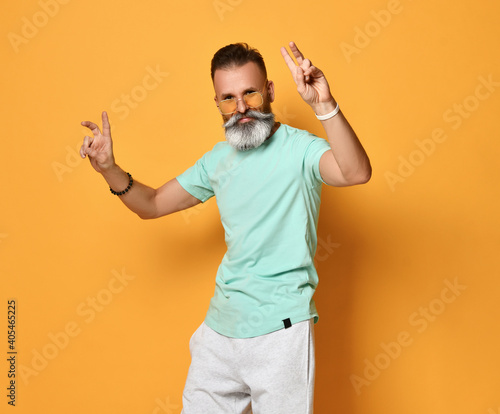 Portrait of a cheerful and stylish middle aged man standing against orange background and showing peace sign. Stylish concept of the elderly. Place for text.